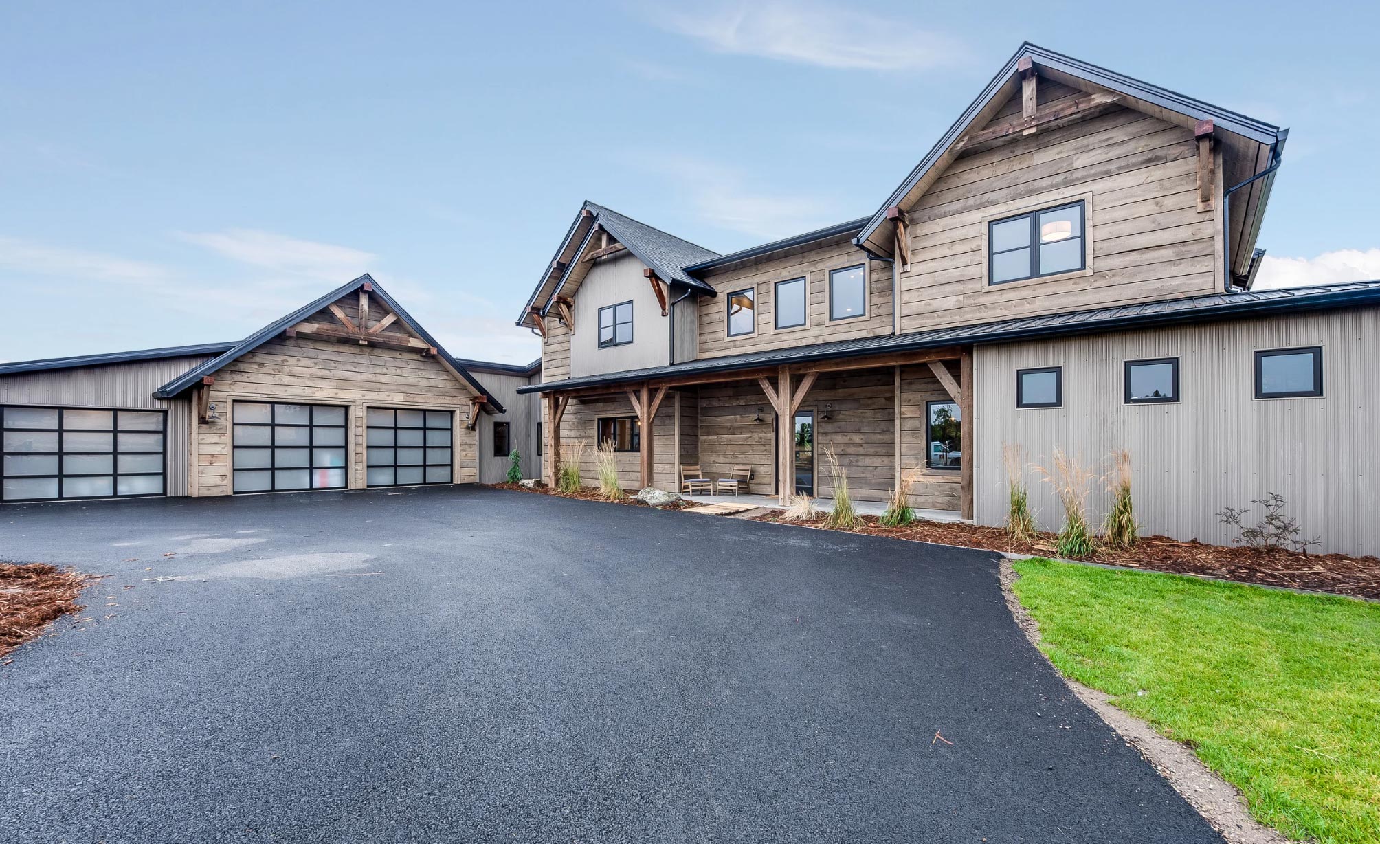Modern rustic house with wood siding, large windows, and a detached three-car garage on an asphalt paving driveway—perfect for those seeking quality Asphalt Paving Services in Delaware.
