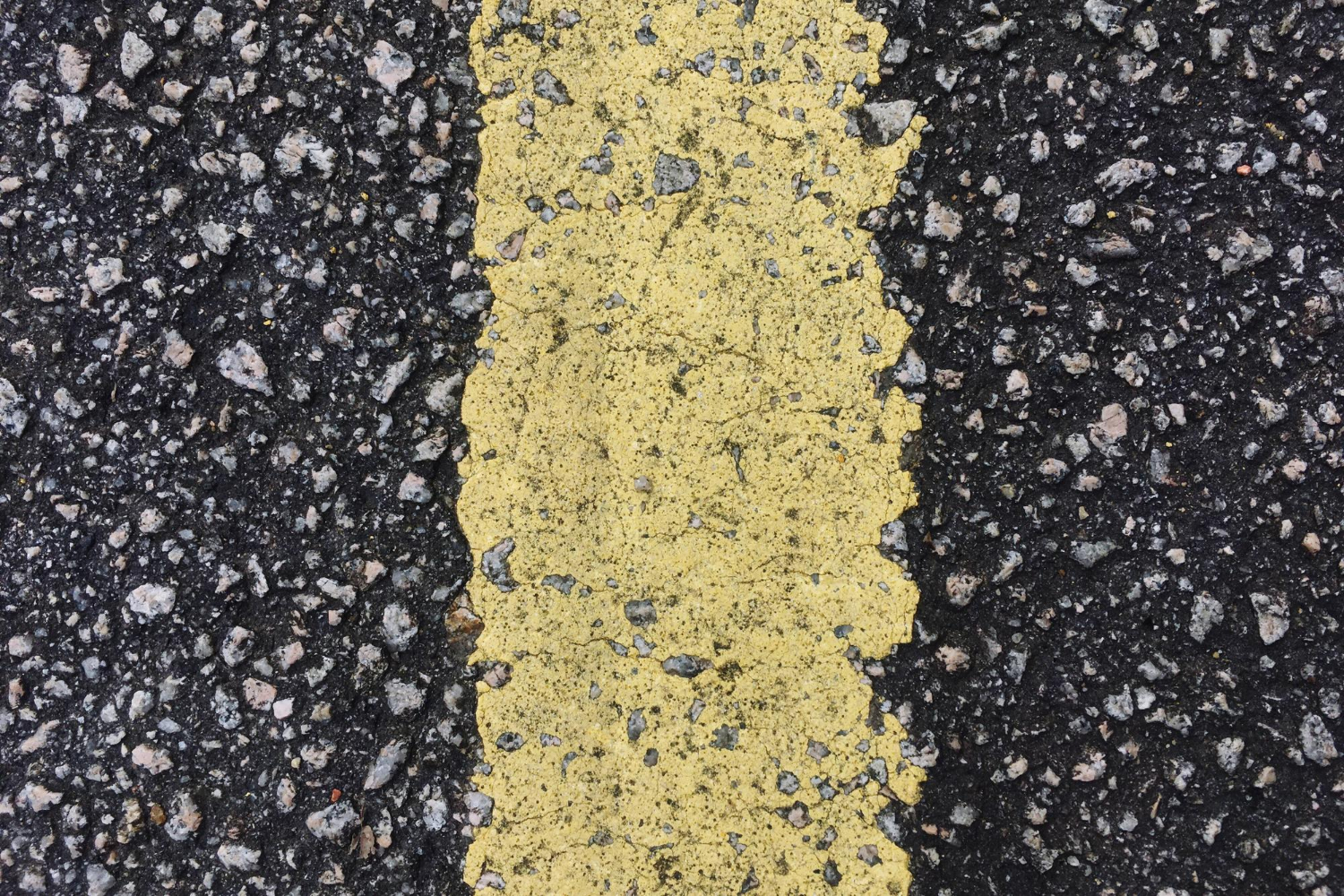 Close-up of a rough, yellow painted line on a textured asphalt road surface.